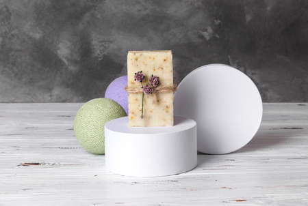 Natural handmade soap on white podium on wooden background with green and lilac balls and gray concrete wall. Hemp rope and paper flowers packaging. Spa organic treatmentの写真素材