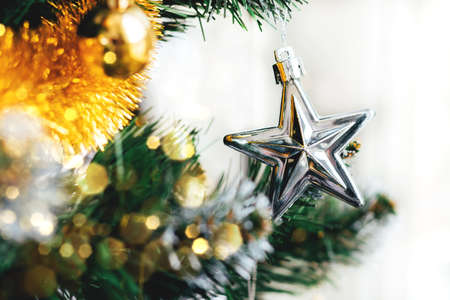 Silver star on decorated Christmas tree with blurred lights bokeh. Holiday card with decorations for...