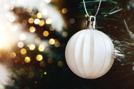 White ball on Christmas tree with blurred lights bokeh. Selective focus. Holiday card with decorations for the New Year's Eveの写真素材