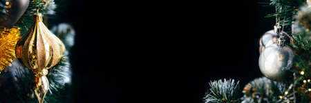 Golden toy and silver ball on Christmas tree with blurred lights bokeh. Wide panoramic holiday two side banner with black copy spaceの写真素材