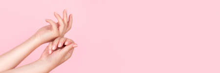 Female hands with beautiful manicure - pink nude nails on pink background, wide panoramic banner with copy space. Nail care conceptの写真素材