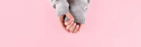 Female hands in gray knitted sweater with beautiful manicure - pink nude nails on pink background, wide panoramic banner with copy space. Nail care conceptの写真素材