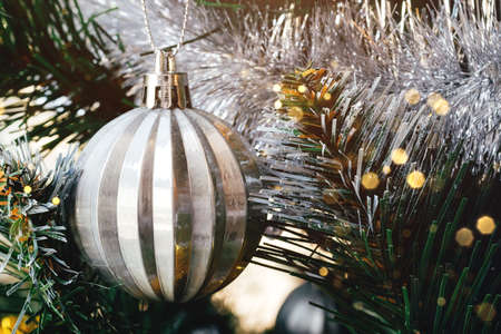 Silver ball on decorated Christmas tree with blurred lights bokeh. Selective focus. Holiday card...