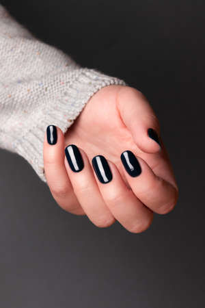 Female hand in gray knitted sweater with beautiful manicure - dark black nails on gray background. Nail care conceptの写真素材