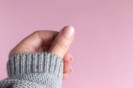 Female hand in gray knitted sweater with beautiful manicure - pink nude nails on pink background. Nail care conceptの写真素材