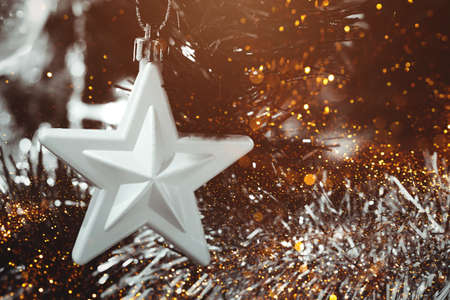 Silver star on Christmas tree with blurred lights bokeh. Selective focus. Holiday card with decorations for the New Years Eveの写真素材