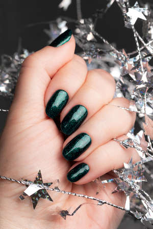 Female hand with beautiful holiday manicure - green glittered nails with silver Christmas twisted...