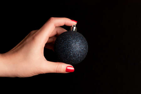 Female hand with blue glittery Christmas ball with beautiful manicure - red nails against black background. Nail and skin care conceptの写真素材