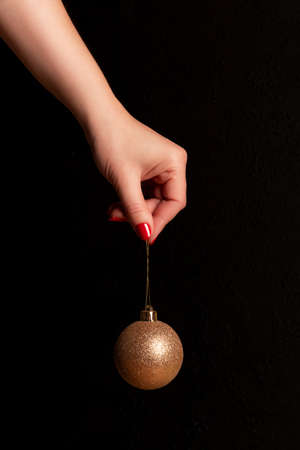 Female hand with golden glittery Christmas ball with beautiful manicure - red nails against black background. Nail and skin care conceptの写真素材