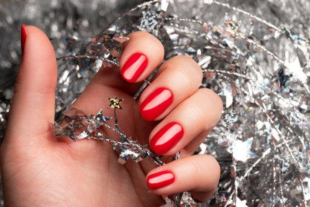 Female hand with beautiful holiday manicure - red nails with silver Christmas twisted wire with...
