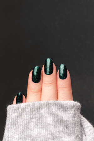 Female hand in gray knitted sweater with beautiful manicure - green glittered nails against gray background. Nail care conceptの写真素材