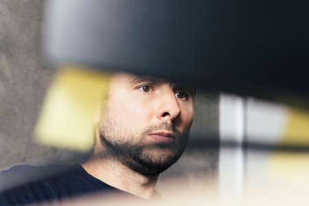 Handsome serious bearded man sitting at the office desk, looking at computer screen with blurred yellow stickers against concrete wall in modern officeの写真素材