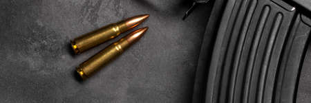 Two bullets and assault rifle on gray concrete background banner, top view panoramic web header....