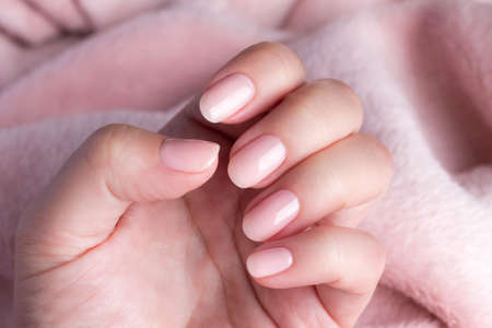 Female hand with beautiful natural manicure - pink nude nails on pale pink fluffy fabric, textile...