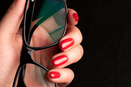 Female hand with beautiful manicure - red nails with glasses on black background closeupの写真素材