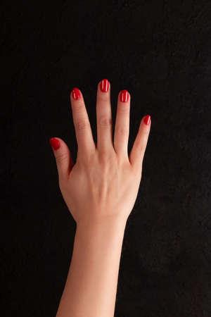 Female hand with beautiful manicure - red nails on dark black backgroundの写真素材