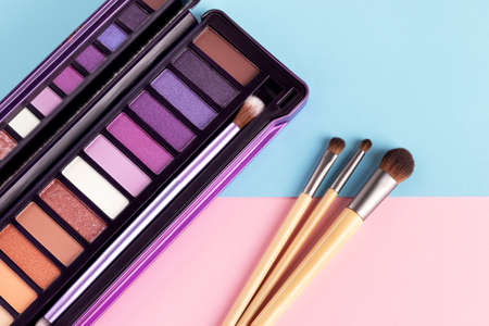 Colorful eye shadow palette and set of makeup brushes on pink and blue background with copy space....