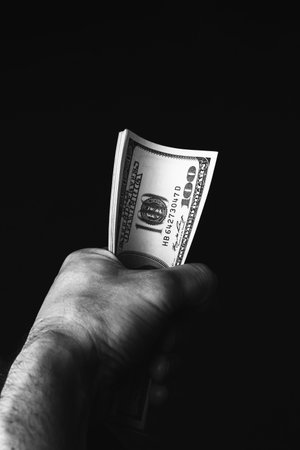 Male hand holding us hundred dollars banknotes on black background. Man with american money closeup....