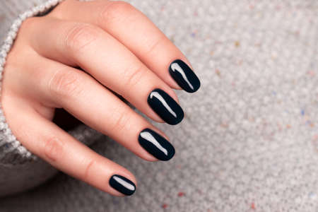 Female hand with beautiful manicure - dark black nails. Nail care concept