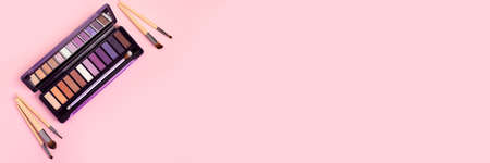 Colorful eye shadow palette and set of makeup brushes on pink background with copy space banner....
