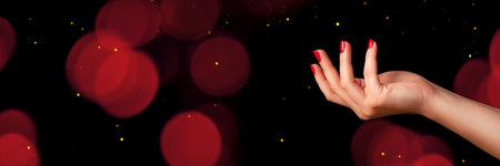 Female hand with beautiful manicure - red nails on dark black background with copy space advertising...