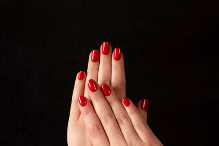 Female hands with beautiful manicure - red nails on dark black background. Nail care conceptの写真素材