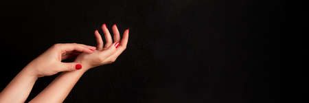 Female hands with beautiful manicure - red nails on dark black background with copy space banner....