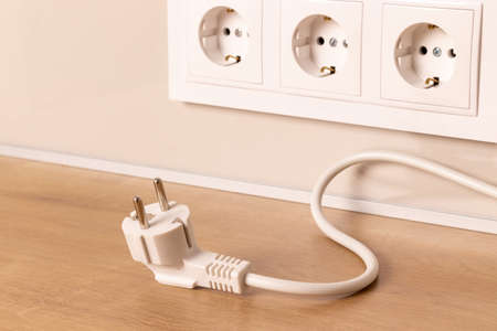 Power cord cable unplugged with group of white european electrical outlets on modern beige wallの写真素材
