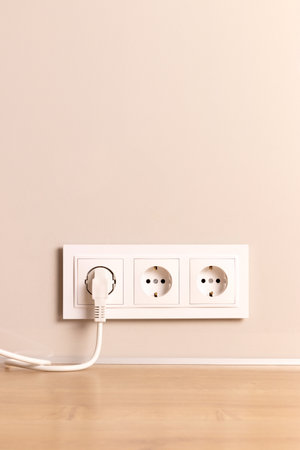 Group of white european electrical outlets with plug inserted into it on modern beige wall with copy spaceの写真素材