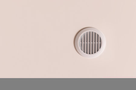 Round air vent with white plastic grate on beige ceiling