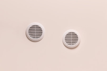 Round air vents with white plastic grate on beige ceilingの写真素材