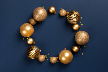 Circle frame of golden Christmas balls and glitter confetti hearts on blue background with copy spaceの写真素材