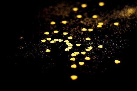 Golden blurred bokeh lights on black background. Glitter sparkle hearts for celebrate. Overlay for your designの写真素材
