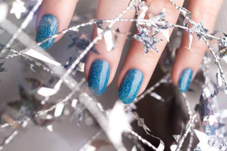 Female hand with beautiful holiday manicure - blue glitter nails with silver twisted wire with stars. Nail care conceptの写真素材