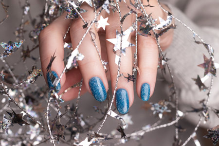 Female hand with beautiful holiday manicure - blue glitter nails with silver Christmas twisted wire with stars. Selective focus. Closeup view. Nail care conceptの写真素材