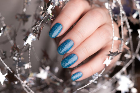Female hand with beautiful holiday manicure - blue glitter nails with silver twisted wire with stars. Nail care conceptの写真素材