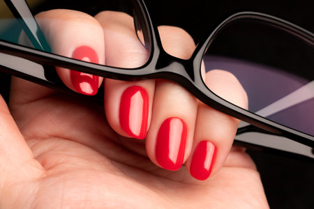 Female hand with beautiful manicure - red nails with glasses on black background closeupの写真素材