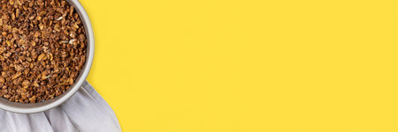 Roasted chocolate granola cereal in round baking tray on bright yellow background banner. Top view, flat lay muesli. Panoramic web header. Wide screen wallpaperの写真素材