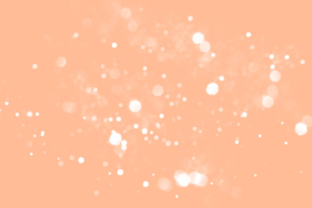 White blurred abstract bokeh lights on peach fuzz background. Snowy shiny glitter sparkle stars for celebrateの写真素材