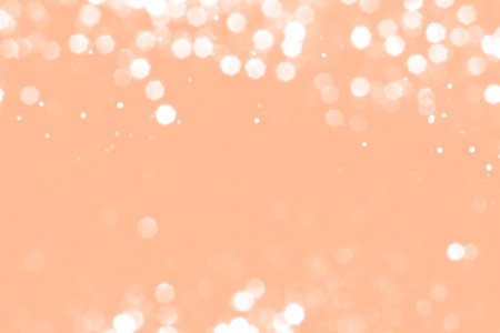 White blurred abstract bokeh lights on peach fuzz background. Snowy shiny glitter sparkle stars for celebrateの写真素材
