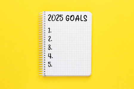 Notebook with 2025 Goals on bright yellow background, spiral bound, checklist, plan.の写真素材