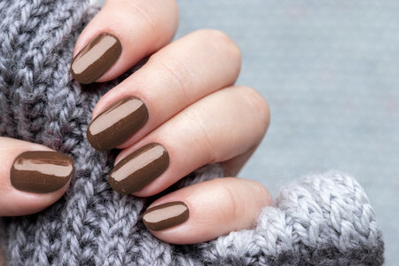Female hand with beautiful trendy manicure - brown, mocha mousse glittered nails. Demonstrating color, trend 2025 year.の写真素材