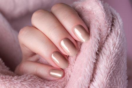 Female hand with beautiful trendy manicure - brown, mocha mousse nails on pale pink fluffy fabric. Nail care concept. Demonstrating color, trend 2025 year.の写真素材