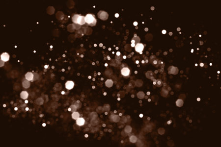 Mocha Mousse, brown blurred abstract bokeh lights on black background. Snowy shiny glitter sparkle stars for celebrate. Demonstrating color, trend 2025 year.の写真素材