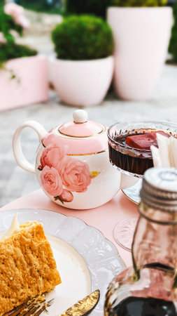 Elegant tea set with floral design, teapot and cup, slice of cake on plate, outdoor background.の写真素材