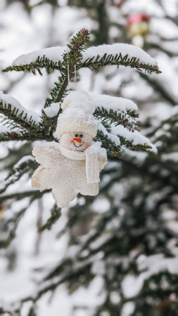 Snowman ornament hanging on snowy tree branch, winter decoration.の写真素材