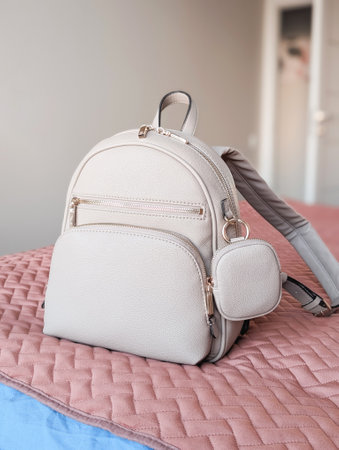 Stylish beige backpack with small pouch on pink quilted bedspread.の写真素材