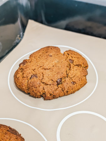 Freshly baked chocolate chip cookie, close-up, warm and soft, placed on baking sheet with parchment paper.の写真素材