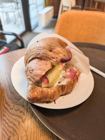 Croissant sandwich with vegetables and fillings on white plate.の写真素材