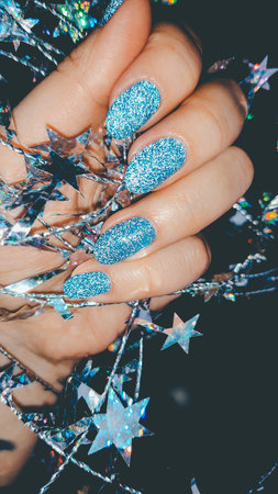 Hand with blue glitter nails holding shiny decorative stars.の写真素材